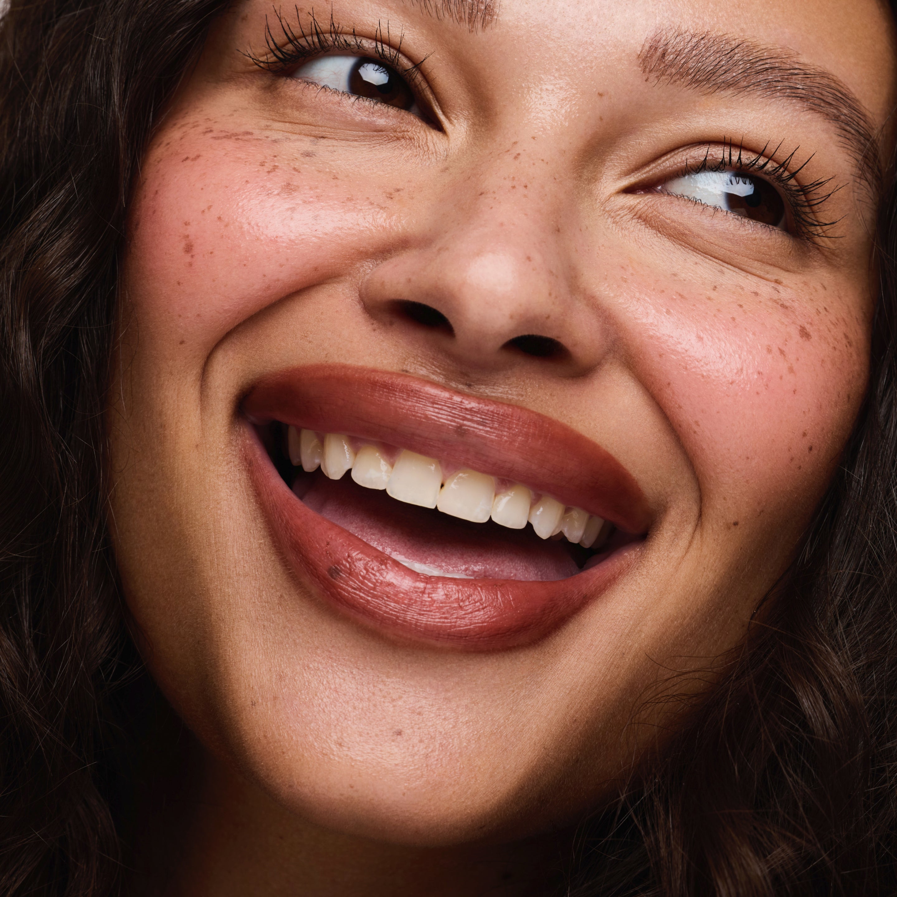 Close-up of a woman's face with a warm smile, wearing a lip liner in a rosy medium brown shade